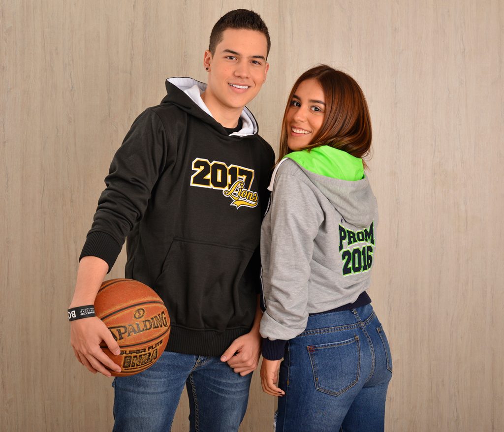 Dos personas con sudaderas negra y gris con capucha junto a un balón.