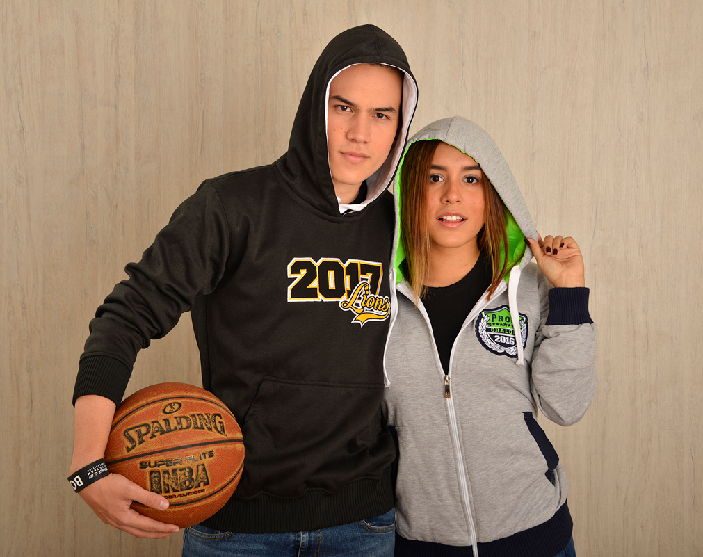 Dos personas con sudaderas negra y gris con capucha junto a un balón.