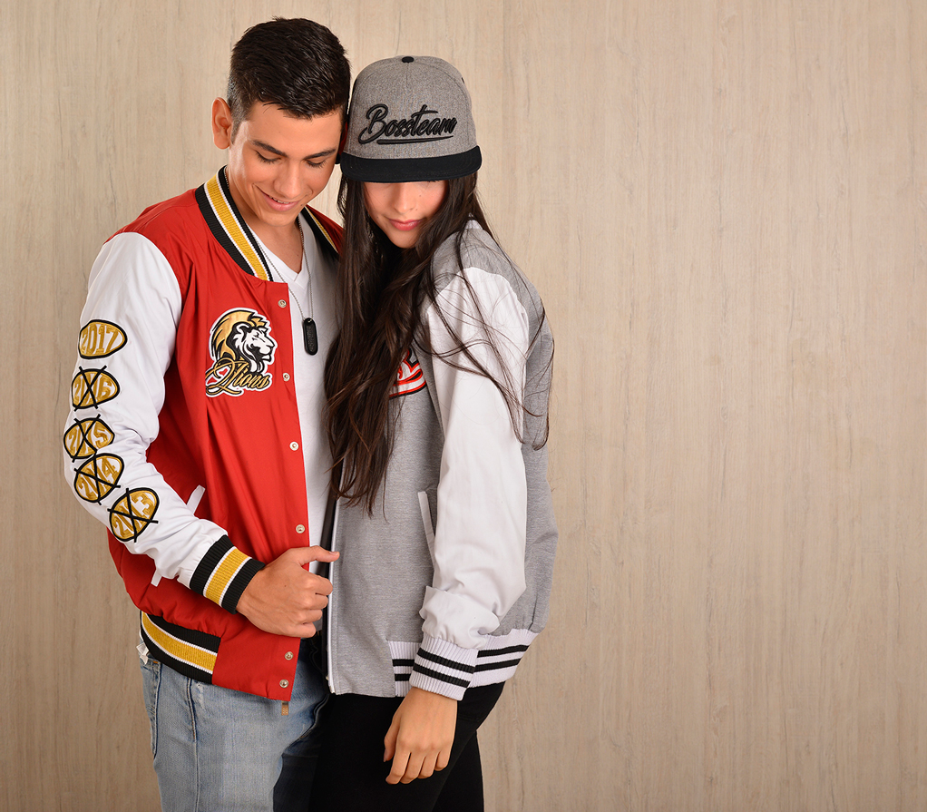 Dos personas muestran chaquetas varsity roja y gris con detalles de equipo.