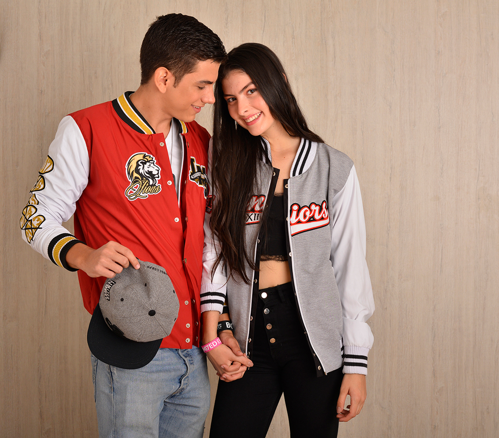 Dos personas con chaquetas varsity roja y gris posan juntas.