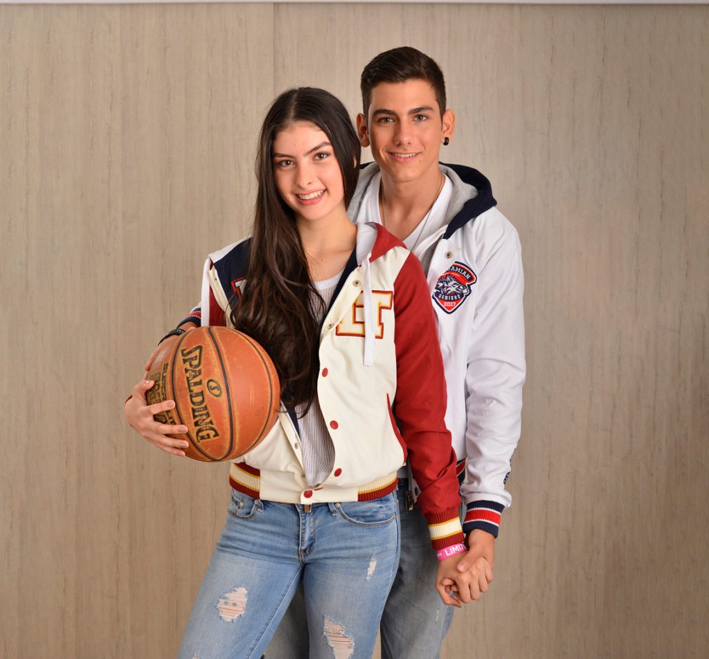Dos personas con chaquetas varsity personalizadas junto a un balón.