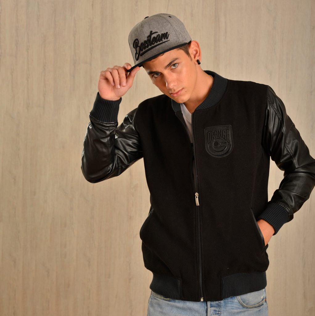 Persona con chaqueta varsity negra de mangas brillantes y una gorra.