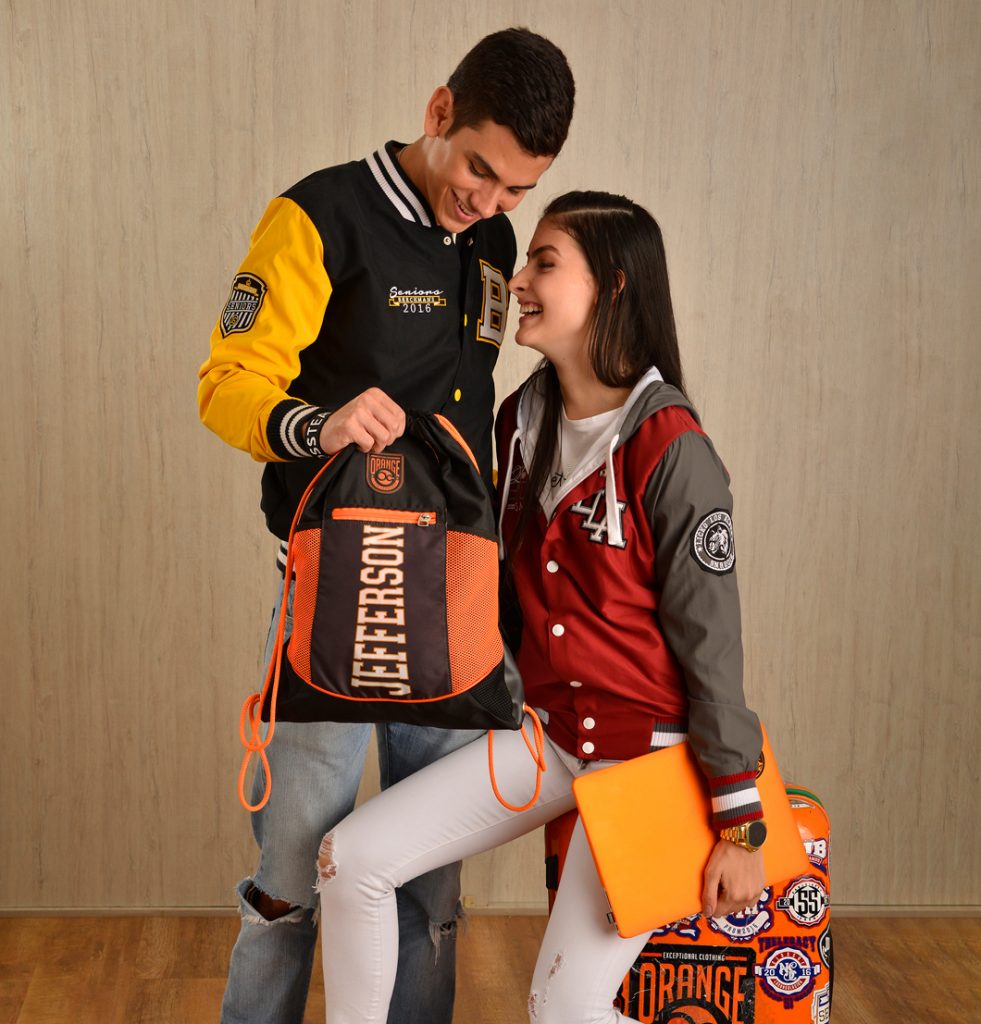 Dos personas con chaquetas varsity junto a una mochila naranja y una carpeta.