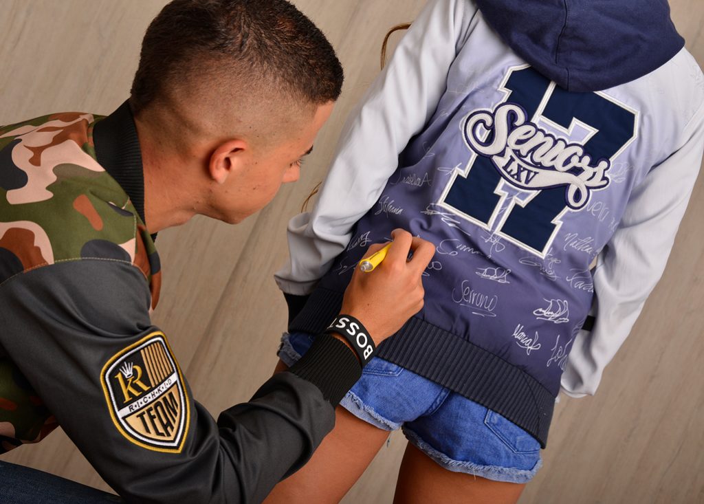 Detalle de una chaqueta personalizada mientras una persona firma el panel posterior.