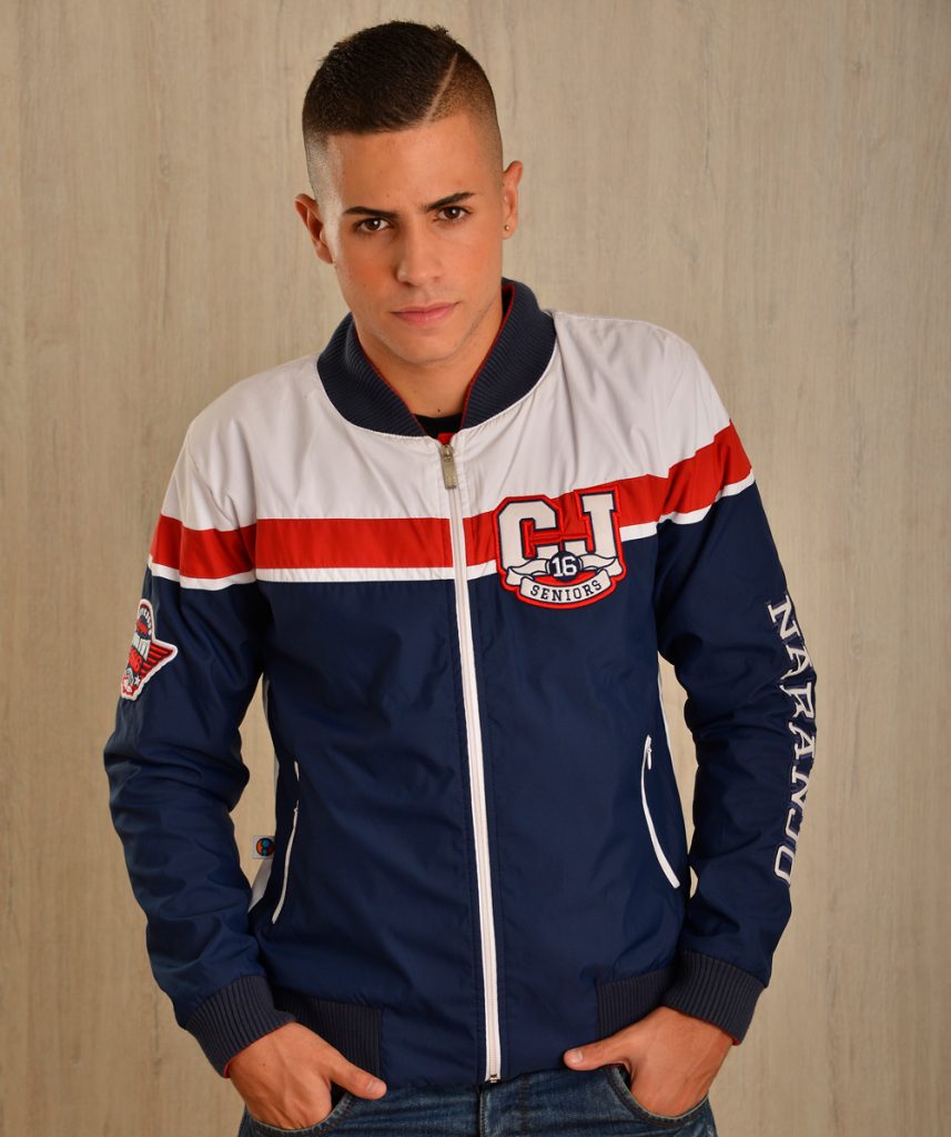 Persona con chaqueta deportiva azul, blanca y roja con emblemas.